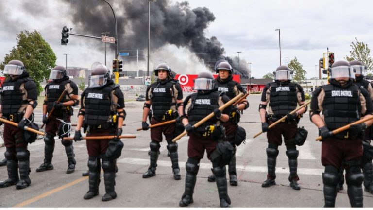 State Police stand guard as smoke billows from buildings that continue to burn in the aftermath of a night of protests and violence following the death of George Floyd, in Minneapolis, Minn., on May 29, 2020. (Charlotte Cuthbertson/The Epoch Times)