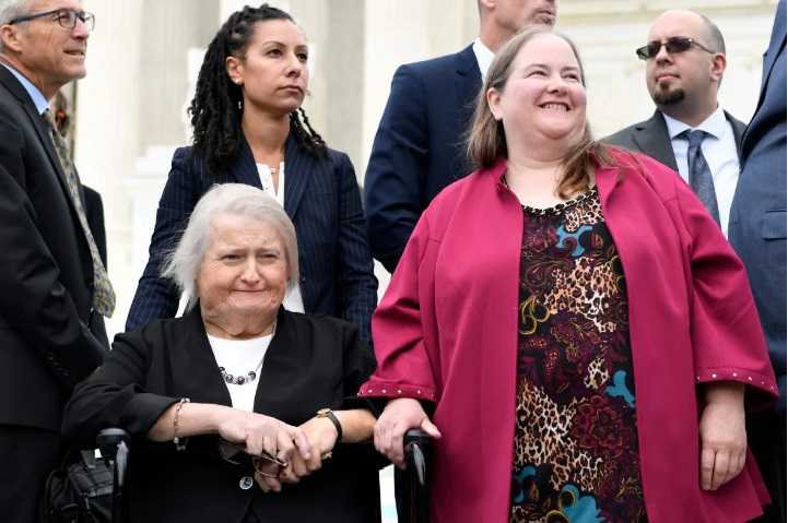 Aimee Stephens, seated, and her wife Donna Stephens, in pink, listen during a news conference outside the Supreme Court on Oct. 8, 2019. Aimee Stephens, who has since died, told CBC she was optimistic the top court would rule in favour of workplace protections for transgender employees. (Susan Walsh/The Associated Press)